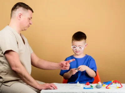 Profissional da saúde interage com uma criança durante uma sessão de jogo terapêutico em uma mesa cercada de brinquedos.