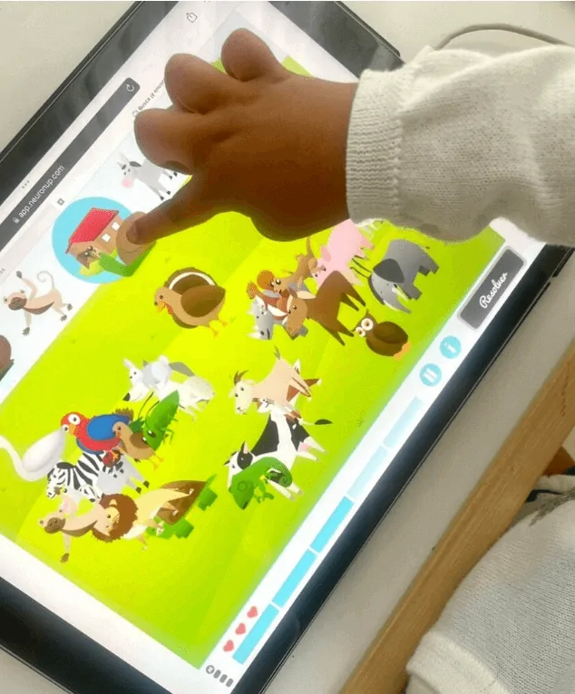 Criança interage com um tablet em uma atividade de categorização de palavras, com imagens de animais e um ambiente rural.