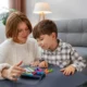 Uma mulher e uma criança interagem durante uma atividade educativa à mesa, em um ambiente doméstico com peças coloridas.