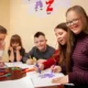 Grupo diverso de alunos e uma docente participam de uma atividade de desenho com marcadores coloridos em uma sala de aula inclusiva.
