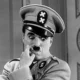 Personagem com bigode característico e uniforme militar em um cenário teatral, junto a gráficos sobre autoritarismo e neuropsicologia.