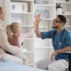 Médico em consulta pediátrica sorri e dá um high five a uma menina, enquanto a mãe observa em um ambiente clínico.