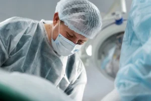 Profissional de saúde com jaleco, máscara e touca cirúrgica realiza mapeamento cerebral intraoperatório em quirófano, paciente acordado.