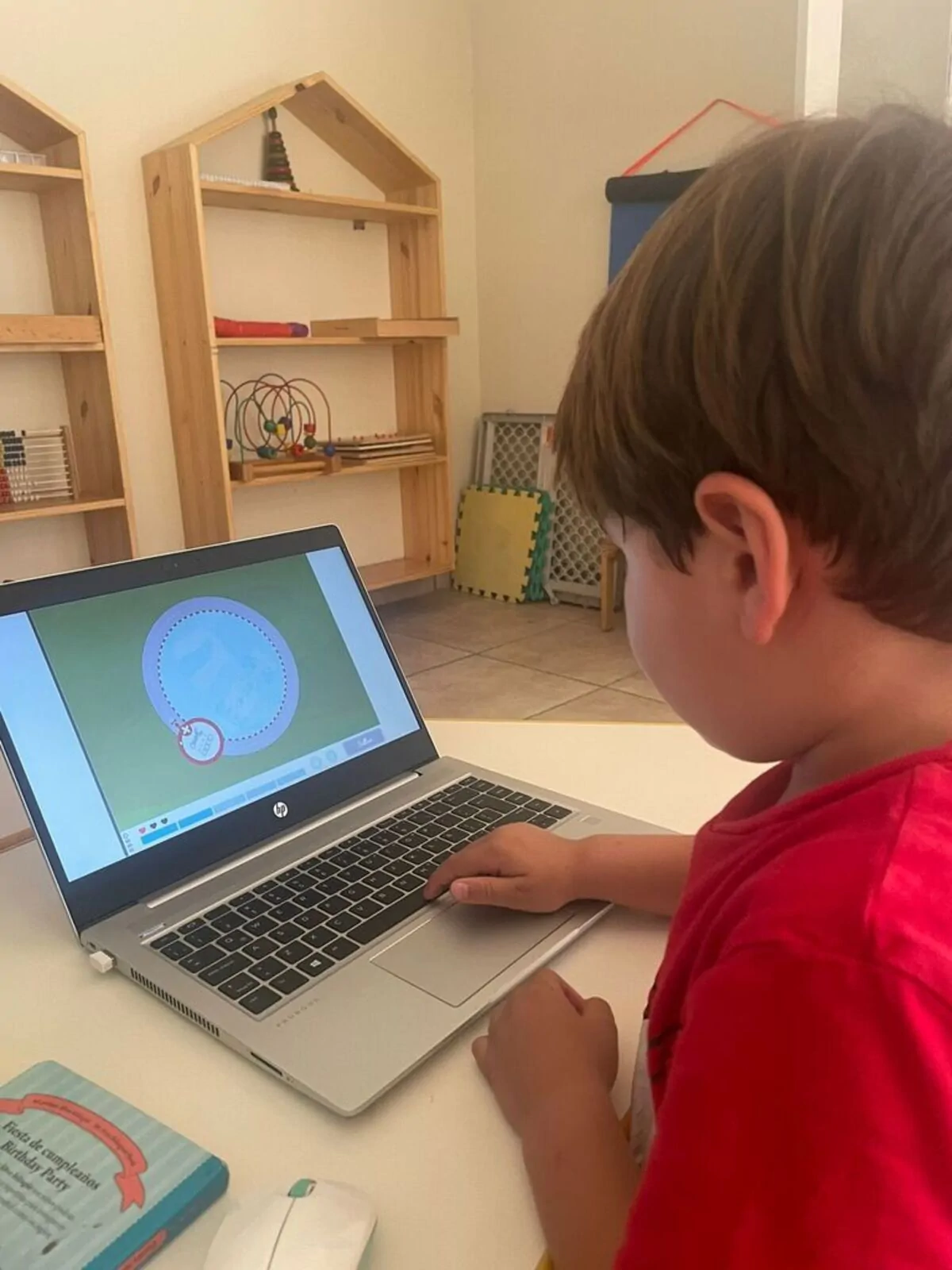 Criança sentada diante de um laptop no Brainkare, usando NeuronUP; a tela mostra uma interface educativa e estantes com brinquedos ao fundo.
