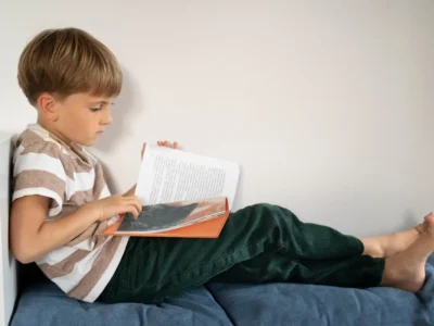 Menino lendo um livro em um sofá, camiseta listrada e ambiente minimalista; foco em consciência fonológica.