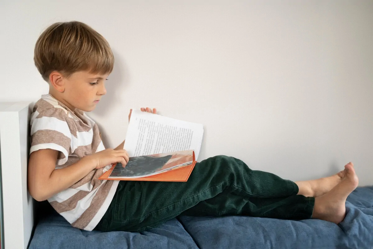 Criança lendo um livro em um sofá, camiseta listrada e ambiente minimalista; foco em consciência fonológica.
