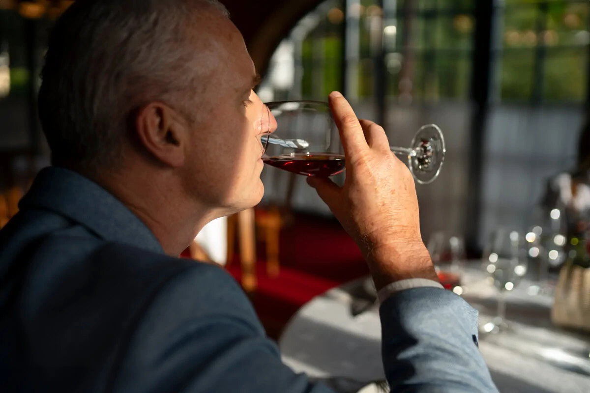 Homem idoso com terno segurando uma taça de vinho em um ambiente elegante, ilustrando a neuropsicologia do álcool.