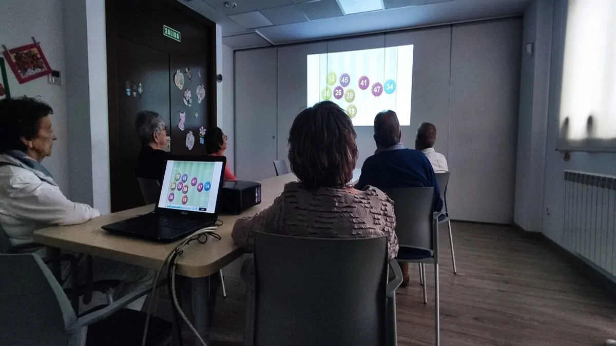 Grupo em sala de aprendizado assistindo a apresentação projetada; tela exibe círculos coloridos com números, com mesas.