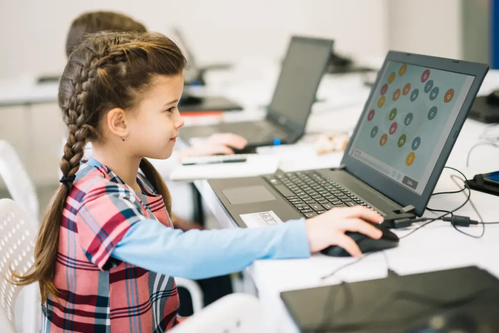 Menina em frente a um laptop em uma sala de aula, explorando atividades da NeuronUP na tela para trabalhar memória e alfabetização.
