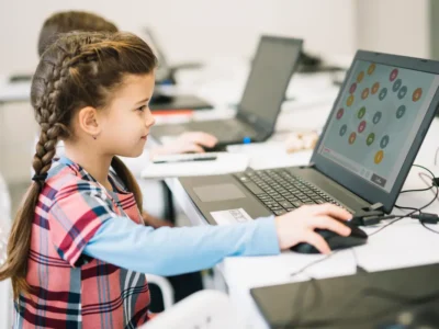Menina em frente a um notebook em uma sala de aula, explorando atividades do NeuronUP na tela para trabalhar memória e alfabetização.
