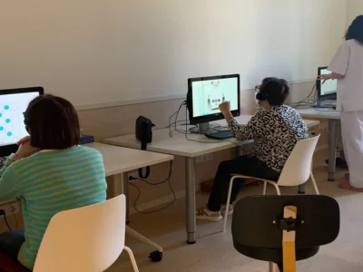 Aula com vários usuários FEM diante de computadores usando NeuronUP, fones de ouvido colocados e uma pessoa em pé supervisionando.