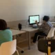 Aula com vários usuários FEM diante de computadores usando NeuronUP, fones de ouvido colocados e uma pessoa em pé supervisionando.