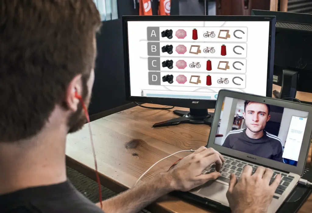 Persona frente a una portátil con auriculares, usando NeuronUP en telerrehabilitación; la pantalla muestra ejercicios.
