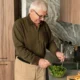 Homem idoso cozinhando em uma cozinha moderna, preparando uma salada com uma tigela e utensílios.