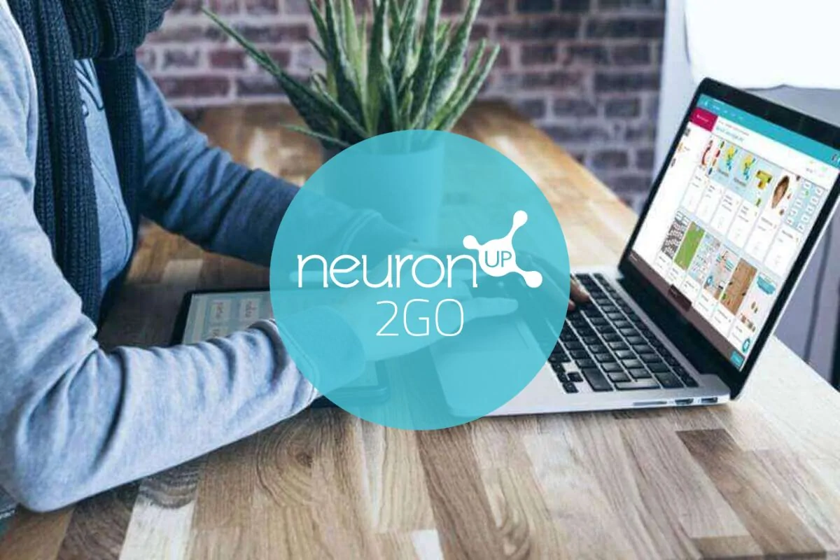 Pessoa usando notebook em mesa de madeira, planta ao fundo, tela exibe NeuronUP 2GO, ambiente com parede de tijolos.