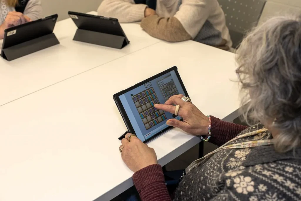 Pessoa usando um tablet durante sessão de estimulação cognitiva com NeuronUP em Elkarkide Iturrama, rodeada por pessoas.