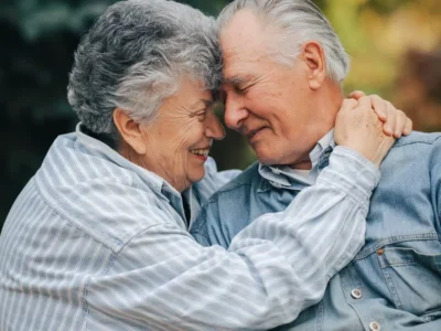 Casal de idosos abraçados ao ar livre, sorrindo, com um tablet para exercícios de reabilitação cognitiva no Dia dos Namorados.