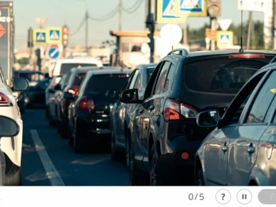 Cena de tráfego urbano com uma fila de carros coloridos em primeiro plano e sinalização viária ao fundo.