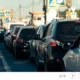 Cena de tráfego urbano com uma fila de carros coloridos em primeiro plano e sinalização viária ao fundo.