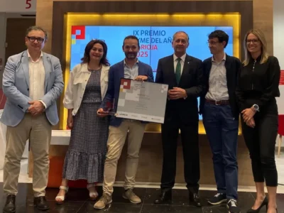 Grupo de pessoas posando em um evento formal; no centro, alguém segura um certificado, em frente a um cartaz vermelho.