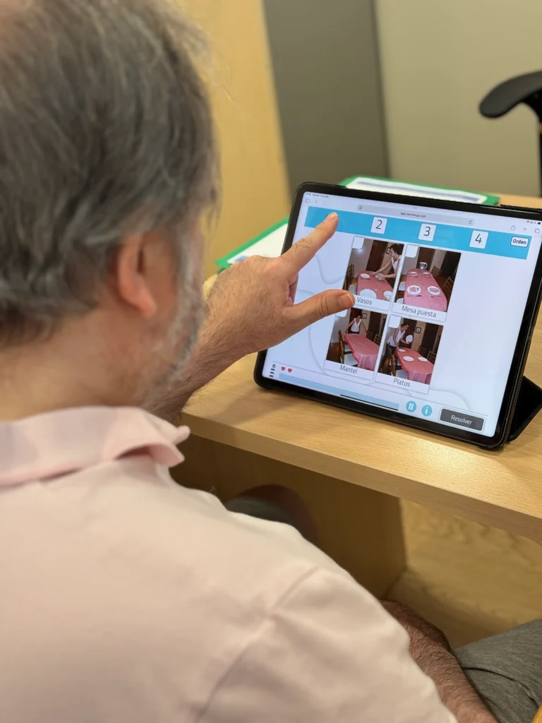 Profissional de neuropsicologia da UEN supervisiona reabilitação no NeuronUP com tablet, mostrando exercícios na tela.