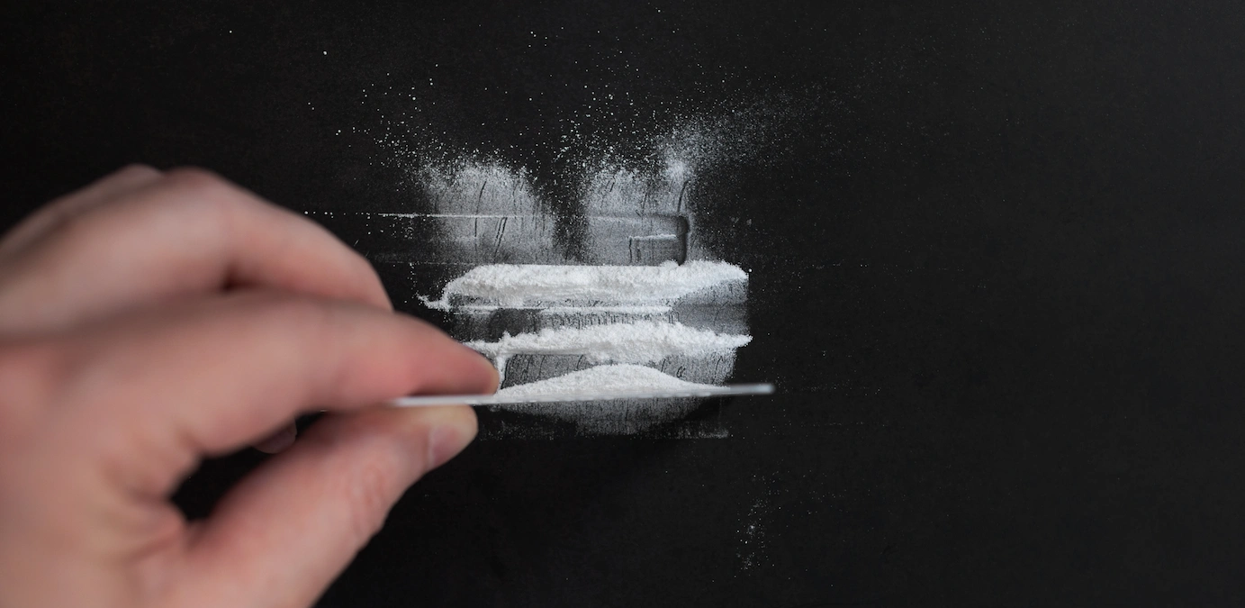 Superfície escura com pó branco disperso; uma mão com cartão alisa o pó, criando padrões sobre o fundo.