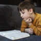 Lehrreiche Illustration eines Kindes, das auf einem Sofa ein Buch liest; Thema: Koexistenz von Autismus und Dyslexie.