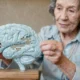 Ältere Frau hält ein hirnförmiges Puzzle und versucht, ein Teil einzusetzen, wodurch die Gehirnkonnektivität hervorgehoben wird.