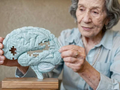 Ältere Frau hält ein hirnförmiges Puzzle und versucht, ein Teil einzusetzen, wodurch die Gehirnkonnektivität hervorgehoben wird.