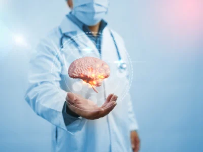 Ärztin oder Arzt im weißen Kittel und mit Maske hält eine beleuchtete dreidimensionale Darstellung eines Gehirns vor einem klinischen oder technologischen Hintergrund.