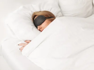 Person im Bett mit schwarzer Schlafmaske und weißer Decke, eine ruhige Szene zur Darstellung von Schlaf und kognitiver Wachheit.