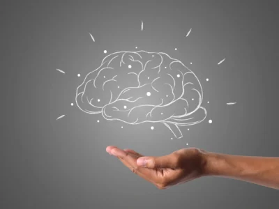 Hand hält ein illustriertes Gehirn mit Energielinien; NeuronUP-Logo vor neutralem Hintergrund.