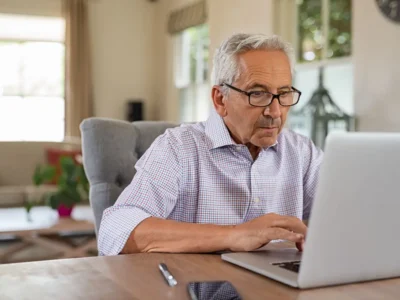 Älterer Mann sitzt konzentriert vor einem Laptop während einer Sitzung zur kognitiven Stimulation mit NeuronUP in einer hellen Umgebung.