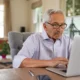 Älterer Mann sitzt konzentriert vor einem Laptop während einer Sitzung zur kognitiven Stimulation mit NeuronUP in einer hellen Umgebung.