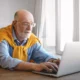 Älterer Mann mit grauem Haar und Bart sitzt in einer modernen Klinik vor einem Laptop und arbeitet konzentriert mit NeuronUP.