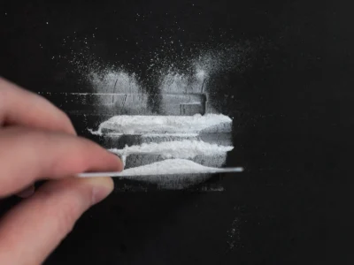 Dunkle Oberfläche mit verstreutem weißem Pulver; eine Hand glättet das Pulver mit einer Karte und erzeugt Muster auf dem Hintergrund.