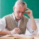 Lehrreiche Illustration: älterer Mann mit Brille sitzt vor Buch und Laptop vor einer grünen Tafel mit Gehirn und ADHS-Diagrammen