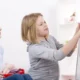 Mädchen interagiert mit einer Tafel, während eine Therapeutin sie in einer pädagogischen Umgebung beobachtet, die die soziale Perspektive veranschaulicht.
