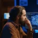 Bärtiger Mann vor einem Computer; auf dem blauen Bildschirm ist eine Gehirngrafik in einer modernen, technologischen Umgebung zu sehen.