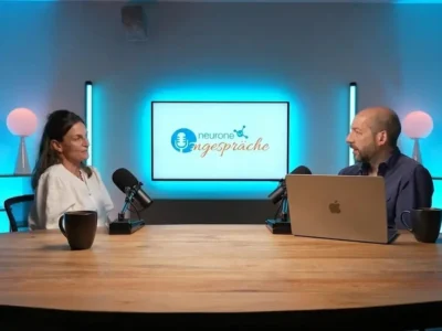 Dr. Genny Lubrini im Gespräch bei NeuronUP Talks in einem Aufnahmestudio mit Mikrofonen und einem Bildschirm mit dem Text Teatro Talks im Hintergrund.