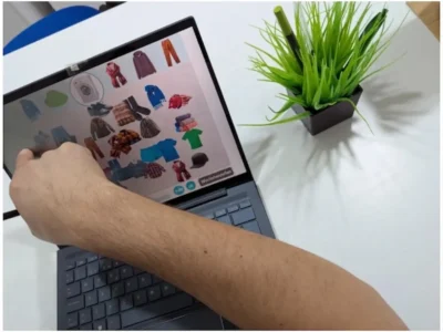 Fachkraft für Psychologie und Neuropsychologie vor einem Laptop auf einem weißen Tisch, auf dem Bildschirm auf Kleidung und eine Pflanze zeigend.