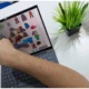 Fachkraft für Psychologie und Neuropsychologie vor einem Laptop auf einem weißen Tisch, auf dem Bildschirm auf Kleidung und eine Pflanze zeigend.
