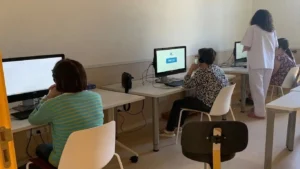 Raum mit mehreren FEM-Nutzerinnen und -Nutzern an Computern, die NeuronUP verwenden und Kopfhörer tragen; eine stehende Person beaufsichtigt sie.