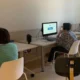 Raum mit mehreren FEM-Nutzerinnen und -Nutzern an Computern, die NeuronUP verwenden und Kopfhörer tragen; eine stehende Person beaufsichtigt sie.
