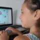 Mädchen sitzt vor einem Laptop, trägt ein Stirnband und arbeitet mit NeuronUP.