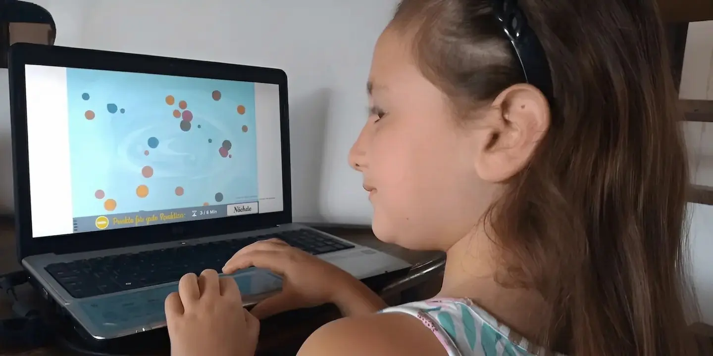 Mädchen sitzt vor einem Laptop, trägt ein Stirnband und arbeitet mit NeuronUP.