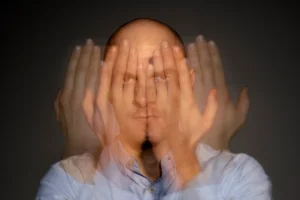 Mann mit rasiertem Kopf und ernstem Gesichtsausdruck, bewegte Hände verschwommen, dunkler Hintergrund, der die Szene hervorhebt.