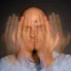 Mann mit rasiertem Kopf und ernstem Gesichtsausdruck, bewegte Hände verschwommen, dunkler Hintergrund, der die Szene hervorhebt.