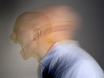 Person mit rasiertem Kopf schreit im Vordergrund, Bewegungseffekt; dunkler Hintergrund.