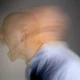 Person mit rasiertem Kopf schreit im Vordergrund, Bewegungseffekt; dunkler Hintergrund.